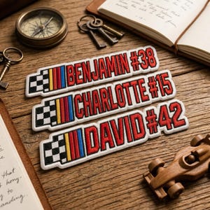 May include: Three rectangular embroidered patches with white borders, each featuring a black and white checkered flag, vertical yellow, red, and blue stripes, and red text reading BENJAMIN #38, CHARLOTTE #15, and DAVID #42 on a white background.