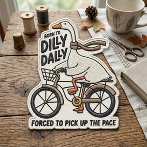 May include: Embroidered patch featuring a goose riding a bicycle with the text "BORN TO DILLY DALLY FORCED TO PICK UP THE PACE." The goose is white with orange feet and a brown scarf. The bicycle is brown and black.