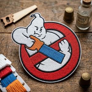 May include: Embroidered patch featuring a cartoon ghost character with an angry expression, holding a blue and orange saw, set against a red circle with a black slash. The patch is surrounded by sewing supplies and a small bottle labeled "Ghost Dust."