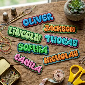 May include: A collection of embroidered name patches featuring bubble-style lettering in various colors including blue, green, orange, and pink. Each patch displays a unique name: Oliver, Lincoln, Jackson, Thomas, Sophia, Camila, and Nicholas.