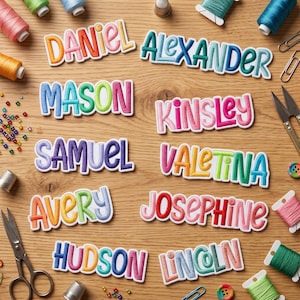 May include: A collection of embroidered name patches featuring the names Daniel, Alexander, Mason, Kinsley, Samuel, Valentina, Avery, Josephine, Hudson, and Lincoln in various colorful fonts, surrounded by sewing supplies like thread and scissors.