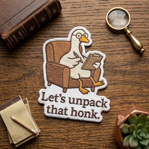 May include: Embroidered patch featuring a cartoon goose wearing glasses and sitting in a brown armchair, holding a clipboard and pen. The patch has the text "Let's unpack that honk." The patch is white with brown, yellow, and black details.