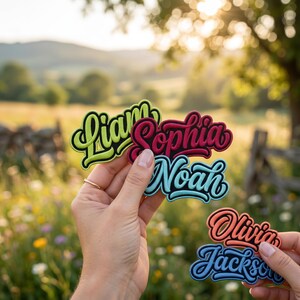 May include: Colorful name patches in various colors, including green, red, blue, and orange. The names are in a stylish script font with a black outline. The background is a blurred outdoor scene with a field and trees.
