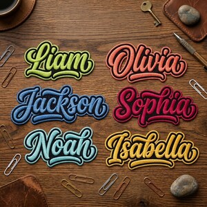 May include: Embroidered name patches in various colors, including green, orange, blue, red, teal, and yellow. Names include Liam, Olivia, Jackson, Sophia, Noah, and Isabella. The patches are on a wooden surface with paper clips and stationery.