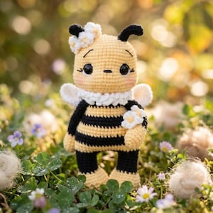 May include: A handmade crochet bee doll with a yellow body, black stripes, and black antennae. The bee has white wings, a white collar, and a flower on its head. The doll is standing in a field of green grass and small purple flowers.