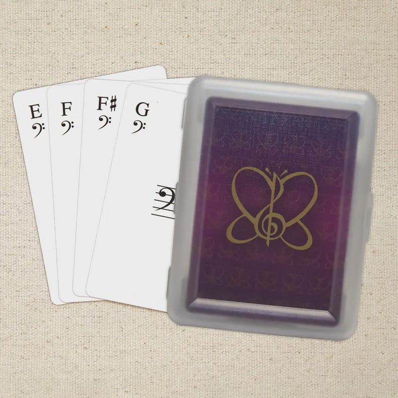 May include: A deck of playing cards with musical notes and a butterfly design. The cards are white with black musical symbols and letters E, F, F#, and G. The card case is purple with a gold butterfly design.