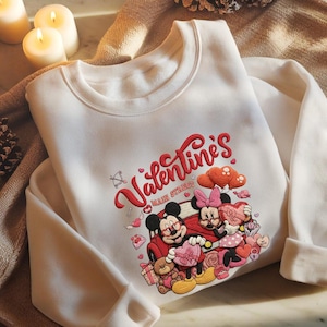 May include: White sweatshirt featuring a Valentine's Day design with Mickey and Minnie Mouse. The design includes the text "Valentine's Main Street" in red script, along with hearts, a car, and teddy bears. A cozy and festive apparel item.