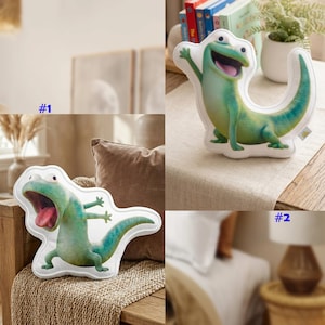 Puede incluir: Dos cojines de peluche con forma de lagarto de dibujos animados en tonos verdes y azules. Un cojín tiene el lagarto con la boca abierta y la lengua fuera. El otro cojín tiene el lagarto saludando. Los cojines están sobre una mesa y un banco.