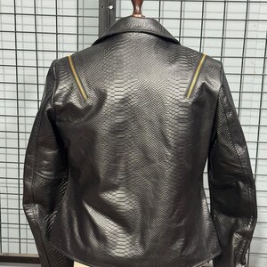 May include: Black faux leather jacket with a snakeskin texture. The jacket features a classic collar, long sleeves, and gold-toned zippers on the shoulders. The back view showcases the jacket's tailored fit and detailed design.