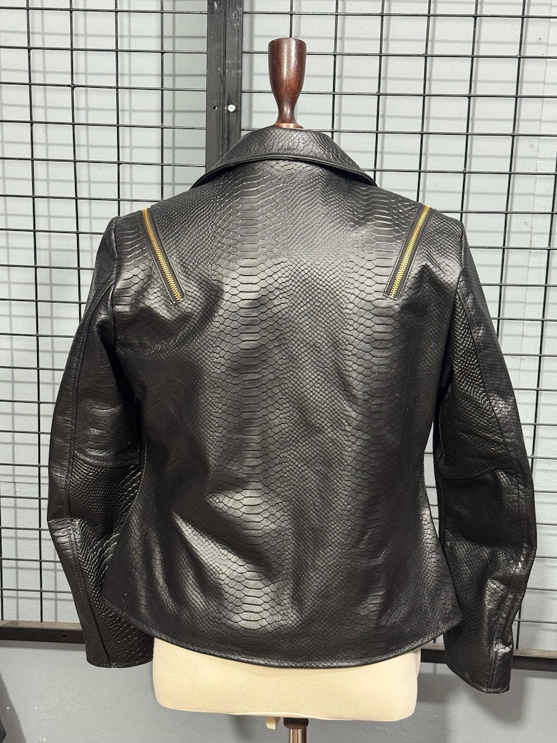 May include: Black faux leather jacket with a snakeskin texture. The jacket features a classic collar, long sleeves, and gold-toned zippers on the shoulders. The back view showcases the jacket's tailored fit and detailed design.