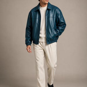 May include: A teal blue leather jacket with a classic collar, front zipper closure, and elasticized cuffs, worn over a cream-colored ribbed knit sweater and light beige pleated trousers, paired with black leather loafers.