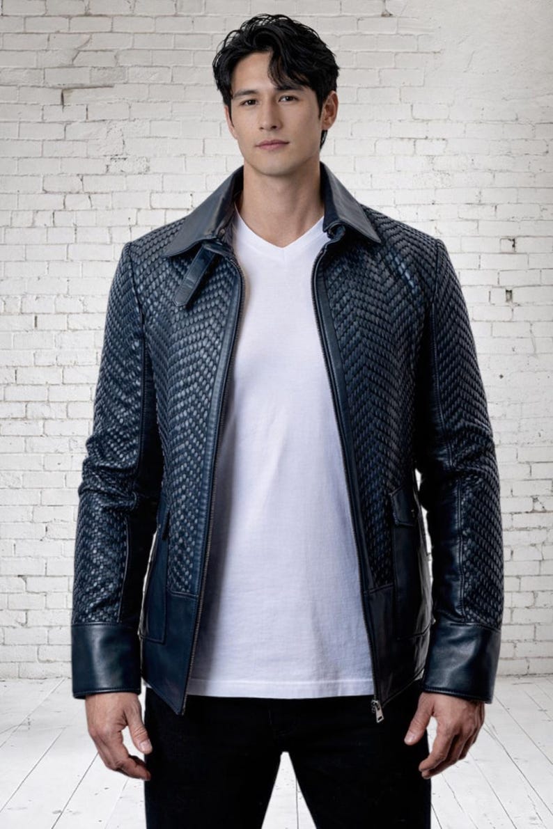 May include: A dark blue jacket featuring a textured, woven chevron pattern on the front and sleeves, a solid collar, and smooth cuffs. The jacket is worn over a plain white V-neck t-shirt and dark trousers, showcasing a structured design.