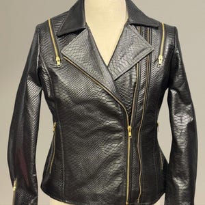 May include: Black faux leather jacket with a snakeskin texture. The jacket has a notched collar, multiple zippered pockets, and gold-coloured zippers. The jacket is displayed on a mannequin.