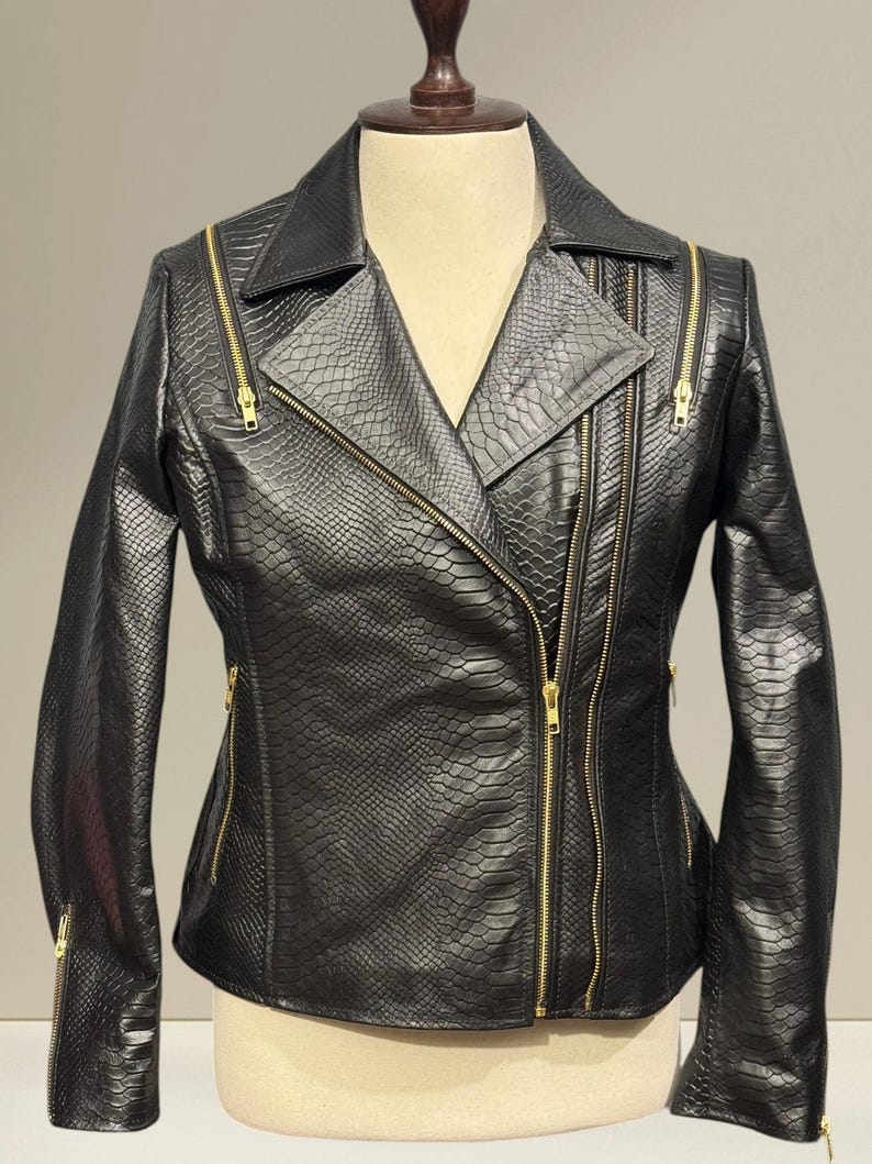 K&ouml;nnte beinhalten: Schwarze Kunstlederjacke mit Schlangenlederstruktur. Die Jacke hat einen Reverskragen, mehrere Rei&szlig;verschlusstaschen und goldfarbene Rei&szlig;verschl&uuml;sse. Die Jacke wird auf einer Schaufensterpuppe pr&auml;sentiert.