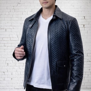 May include: A navy blue quilted leather jacket with a zipper closure, two front pockets, and a notched collar. The jacket is worn over a white V-neck shirt and black pants. The jacket's design features a subtle, textured pattern.