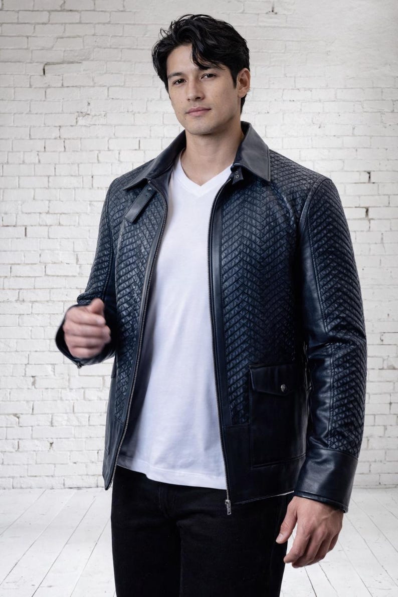 May include: A dark navy blue jacket featuring a quilted chevron pattern on the chest and sleeves, a pointed collar, a full-length front zipper, and two lower flap pockets with snap closures, worn over a plain white V-neck shirt and black pants.