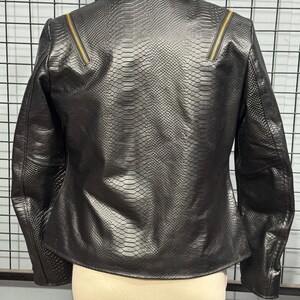 May include: Black faux leather jacket with a snakeskin texture. The jacket features a notched collar, a zipper detail on each shoulder, and a tailored fit. The back view of the jacket is displayed on a mannequin.