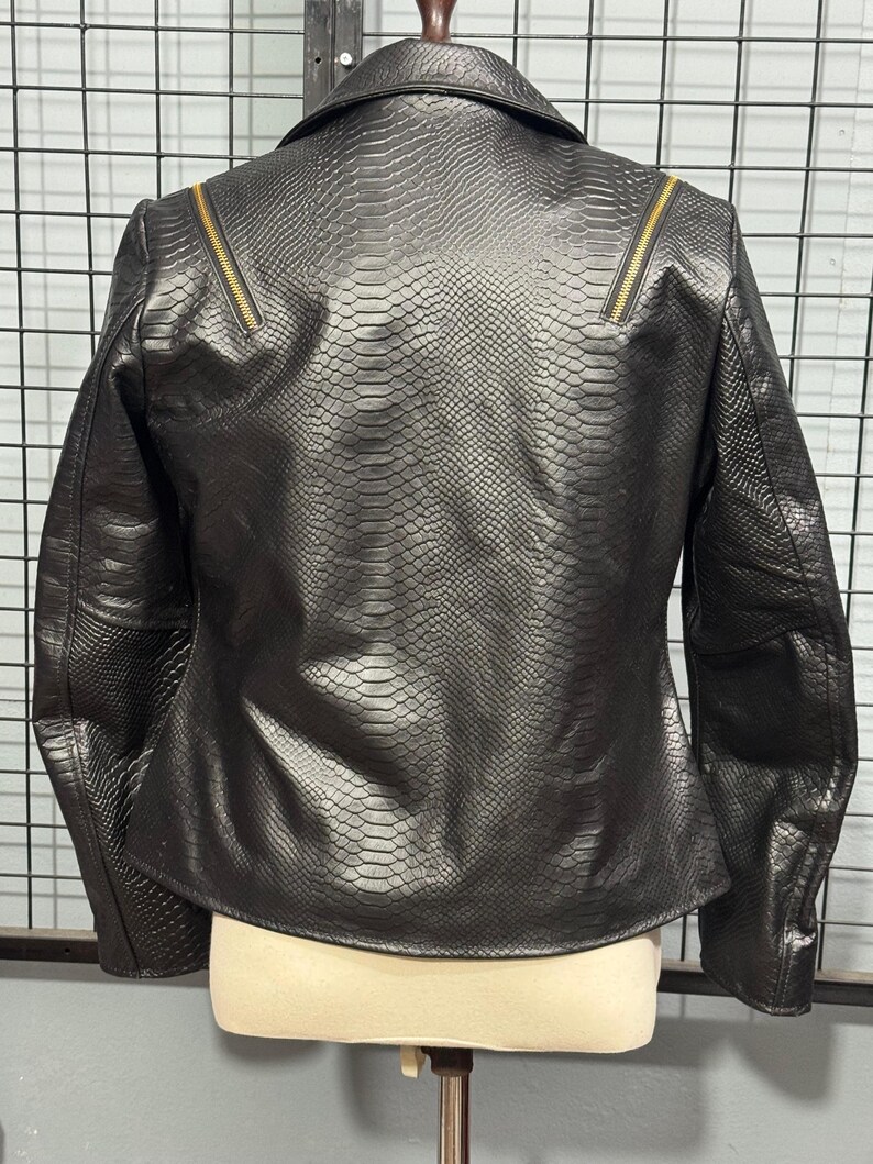 May include: Black faux leather jacket with a snakeskin texture. The jacket features a notched collar, a zipper detail on each shoulder, and a tailored fit. The back view of the jacket is displayed on a mannequin.