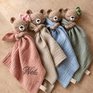 Puede incluir: Cuatro mantitas de apego de oso tejidas a ganchillo en rosa empolvado, beige, azul claro y verde salvia. Cada oso tiene una cara bordada y un pequeño lazo de tela. La manta rosa lleva el nombre Nela bordado. Cada manta tiene una etiqueta.