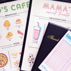 K&ouml;nnte beinhalten: Caf&eacute;-Men&uuml; mit Fr&uuml;hst&uuml;cks-, Pizza- und Smoothie-Optionen. Das Men&uuml; befindet sich in einem schwarzen, ledergebundenen Einband. Ein G&auml;stebon und ein schwarzer Rechnungsordner mit dem Wort "Danke" sind ebenfalls zu sehen.