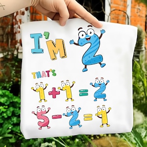 May include: White tote bag with cartoon numbers and the phrases "I'M" and "THAT'S". The numbers are in various colours and depict simple maths equations, including addition and subtraction problems. The bag is held by a hand.