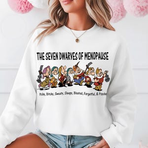 May include: White sweatshirt featuring a graphic of the Seven Dwarves with the text "THE SEVEN DWARVES OF MENOPAUSE" above them. Below the dwarves are the words "Itchy, Bitchy, Sweaty, Sleepy, Bloated, Forgetful, & Psycho."