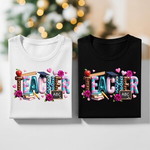 May include: Two t-shirts, one white and one black, each featuring the word "TEACHER" in a colorful, decorative font. The design includes an apple, ruler, graduation cap, hearts, flowers, books, a pencil, and an ABC chalkboard.