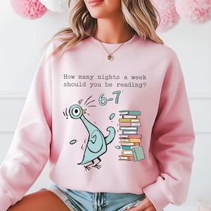May include: Pink sweatshirt with a cartoon pigeon and a stack of books. The text on the shirt reads, "How many nights a week should you be reading?" with the answer "6-7".