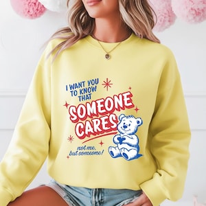 May include: A yellow sweatshirt featuring the text "I WANT YOU TO KNOW THAT SOMEONE CARES" in blue and red, with a cartoon bear graphic. The phrase "not me, but someone!" is also included. The sweatshirt is a solid yellow colour.