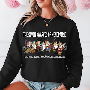 May include: Black sweatshirt featuring the phrase "THE SEVEN DWARVES OF MENOPAUSE" above a cartoon image of seven dwarves. Below the text are the words "Itchy, Bitchy, Sweaty, Sleepy, Bloated, Forgetful, & Psycho."