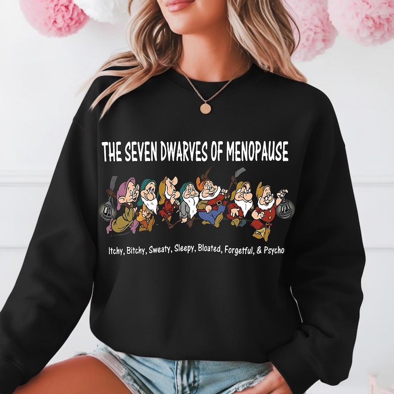 May include: Black sweatshirt featuring the phrase "THE SEVEN DWARVES OF MENOPAUSE" above a cartoon image of seven dwarves. Below the text are the words "Itchy, Bitchy, Sweaty, Sleepy, Bloated, Forgetful, & Psycho."