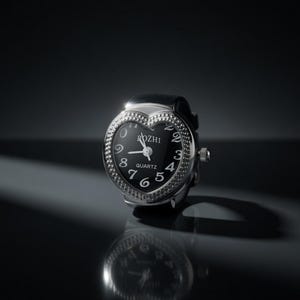 May include: A heart-shaped ring watch with a black face and silver bezel. The watch face displays white numerals and hands, with the brand name "ROZHI" at the top. The watch is set against a dark background, with a reflection visible below.
