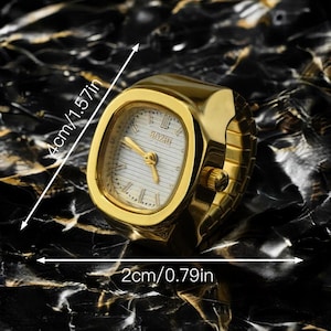May include: A gold-toned ring watch with a rectangular face, measuring 4cm (1.57in) by 2cm (0.79in). The watch face is white with black Roman numerals and gold hands. The band is a flexible, expandable design.