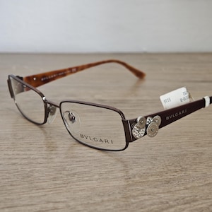 Puede incluir: Una taza de cerámica blanca con un asa negra y el texto "But First, Coffee" en negrita negra. La taza está sobre una superficie de madera. La taza mide aproximadamente 10 cm de alto.