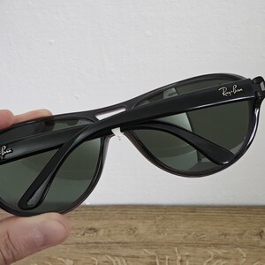 Puede incluir: Gafas de sol negras con lentes verde oscuro. El logotipo de Ray-Ban es visible en las patillas. Las gafas de sol tienen un dise&ntilde;o cl&aacute;sico y deportivo, adecuado para actividades al aire libre. La montura es negra brillante.