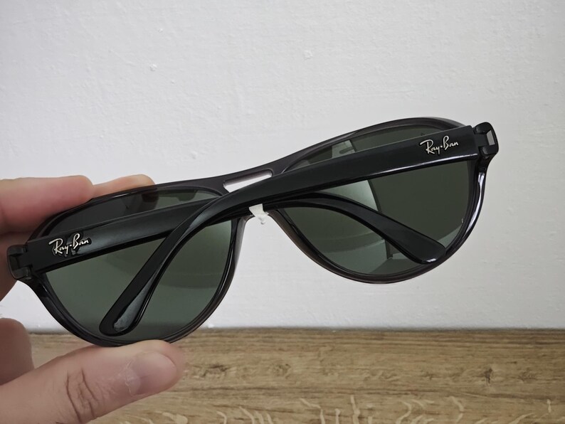 Puede incluir: Gafas de sol negras con lentes verde oscuro. El logotipo de Ray-Ban es visible en las patillas. Las gafas de sol tienen un dise&ntilde;o cl&aacute;sico y deportivo, adecuado para actividades al aire libre. La montura es negra brillante.