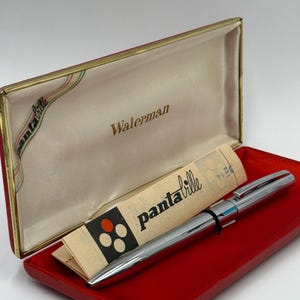 K&ouml;nnte beinhalten: Ein silberner Waterman-Stift in einem roten Etui mit cremefarbenem Innenraum. Das Etui ist ge&ouml;ffnet und zeigt den Stift und einen Papiereinsatz mit dem Text "pantaville". Der Stift liegt auf einer roten Oberfl&auml;che.