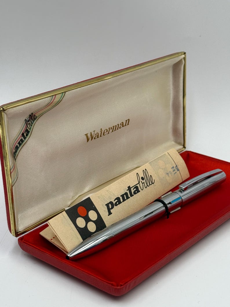 K&ouml;nnte beinhalten: Ein silberner Waterman-Stift in einem roten Etui mit cremefarbenem Innenraum. Das Etui ist ge&ouml;ffnet und zeigt den Stift und einen Papiereinsatz mit dem Text "pantaville". Der Stift liegt auf einer roten Oberfl&auml;che.