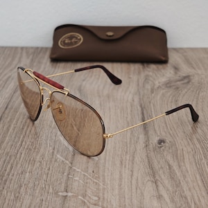 K&ouml;nnte beinhalten: Sonnenbrille im Aviator-Stil mit goldfarbenem Gestell und braunen Gl&auml;sern. Die Sonnenbrille hat einen braunen Steg und B&uuml;gel und wird mit einem braunen Lederetui geliefert.