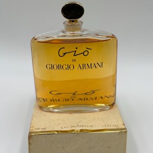 May include: A clear glass bottle of Giorgio Armani Gio perfume, filled with a golden-colored liquid. The bottle has a gold-colored cap and is labeled with the brand name and fragrance name. The box reads "100 mL" and "3.4 fl. oz."