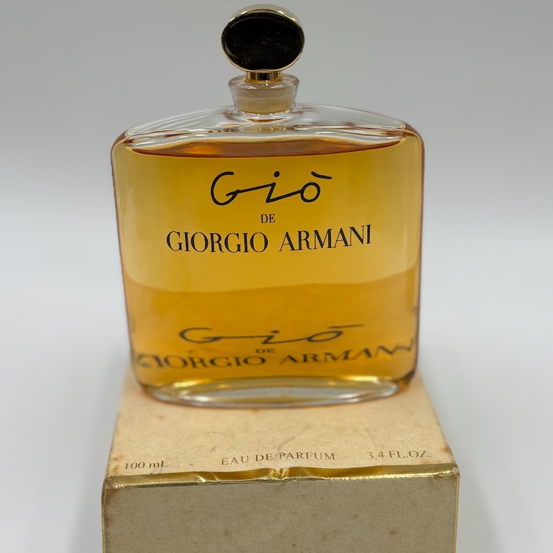 May include: A clear glass bottle of Giorgio Armani Gio perfume, filled with a golden-colored liquid. The bottle has a gold-colored cap and is labeled with the brand name and fragrance name. The box reads "100 mL" and "3.4 fl. oz."