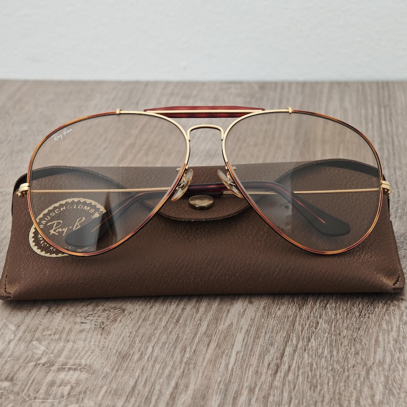 K&ouml;nnte beinhalten: Ray-Ban Aviator-Brille mit goldfarbenem Rahmen und braunen Schildpatt-Akzenten. Die Brille liegt auf einem braunen Lederetui mit dem Ray-Ban-Logo.
