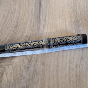 以下が含まれることがあります： 黒とシルバーのペン、華やかなフローラルデザイン。 ペンの長さは約13cm。 ペンには黒いキャップとペン先の近くに透明な部分があります。 ペンの横にはメジャーがあります。