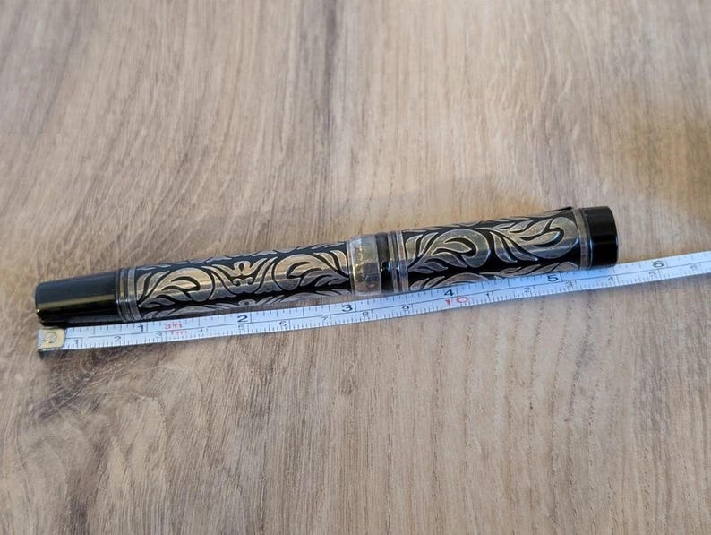 以下が含まれることがあります： 黒とシルバーのペン、華やかなフローラルデザイン。 ペンの長さは約13cm。 ペンには黒いキャップとペン先の近くに透明な部分があります。 ペンの横にはメジャーがあります。