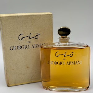 May include: A clear glass perfume bottle filled with amber liquid, featuring a black cap and the text "Gi&ograve; DE GIORGIO ARMANI" printed on the front. Beside it stands a rectangular, off-white cardboard box with the same brand text.