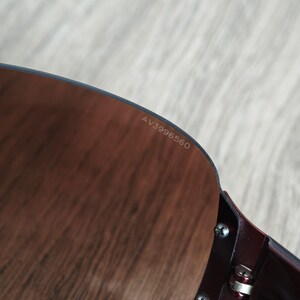May include: Close-up of sunglasses with a dark burgundy frame and brown-tinted lenses. The text "AV3996560" is printed on the lens. The sunglasses are partially visible, showing the frame's hinge and screws.