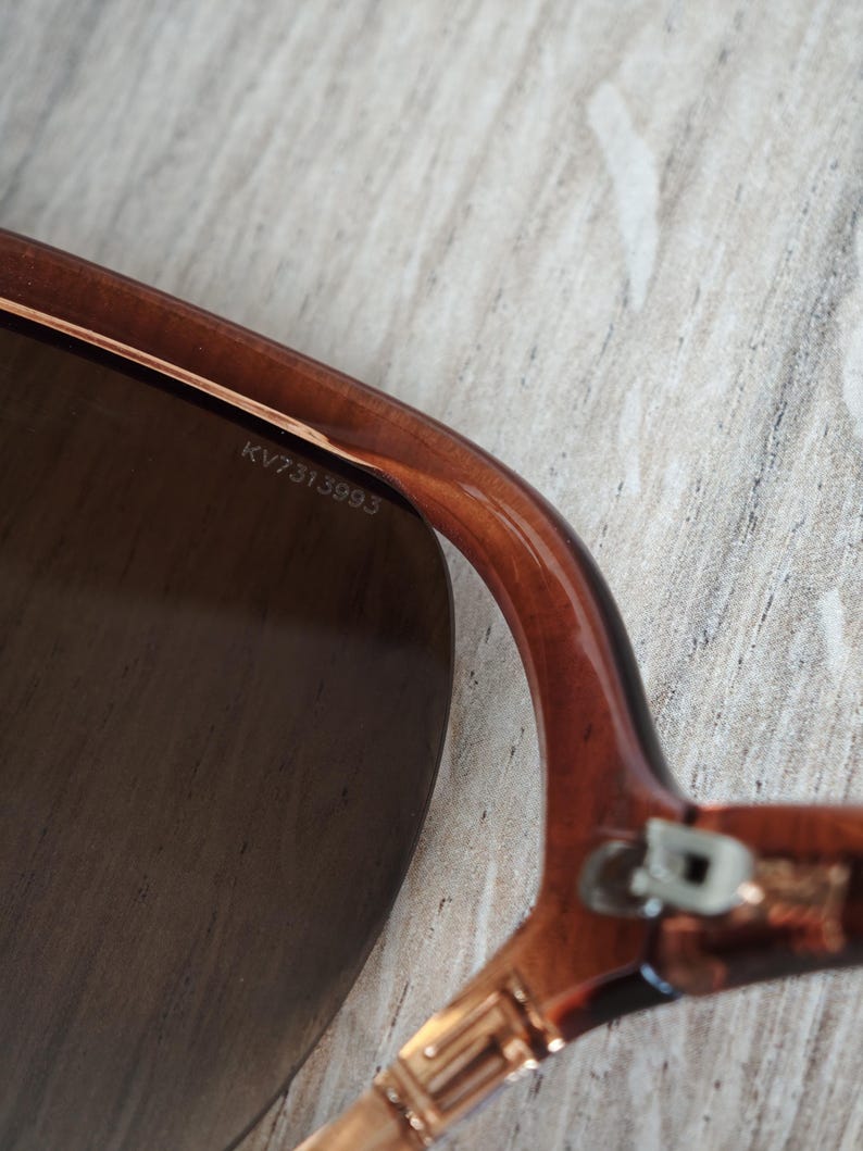 Puede incluir: Primer plano de gafas de sol marrones con una lente oscura. La montura es de color marr&oacute;n transl&uacute;cido. El texto "KV7313993" est&aacute; impreso en el interior de la montura.