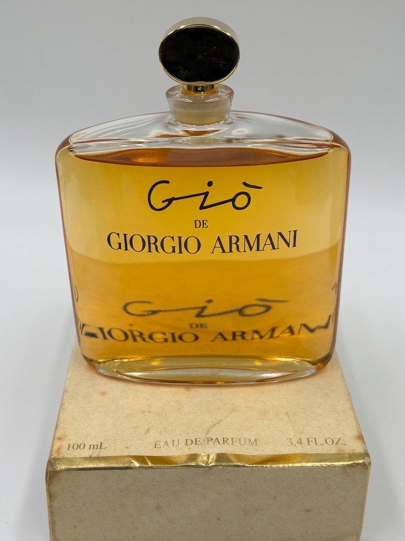 May include: A rectangular glass bottle of Giorgio Armani Gi&ograve; perfume. The bottle contains a golden-colored liquid and is topped with a gold-colored cap. The label reads "Gi&ograve; de Giorgio Armani". The box reads "100 mL" and "3.4 FL.OZ."