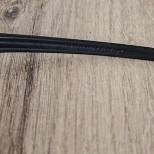 May include: Close-up of a black object with the text "MADE IN U.S.A." embossed on its surface. The object is set against a light brown wooden background.