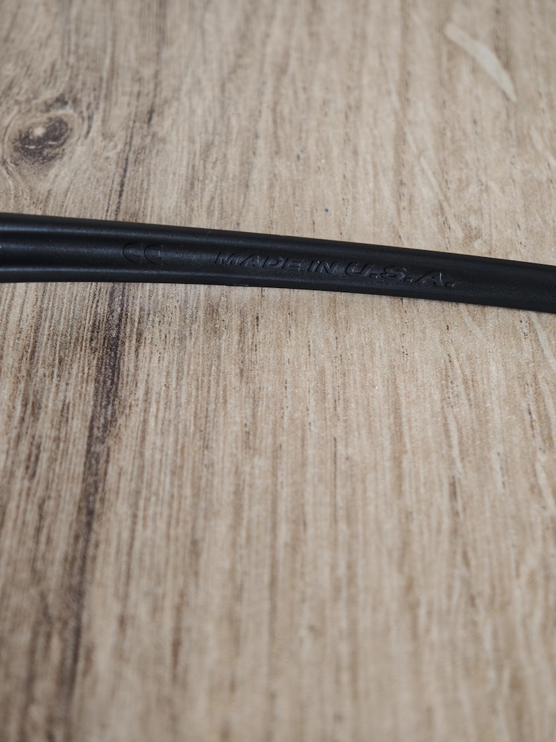 May include: Close-up of a black object with the text "MADE IN U.S.A." embossed on its surface. The object is set against a light brown wooden background.